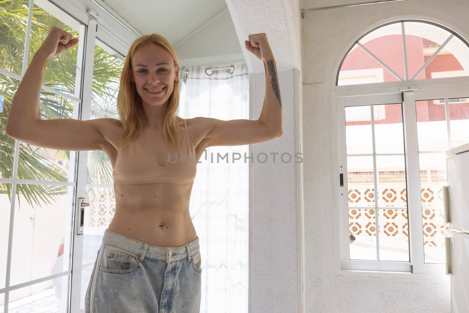a happy girl of European appearance stands in a house in big jeans and shows the result of losing weight and proper nutrition.healthy lifestyle concept. High quality photo