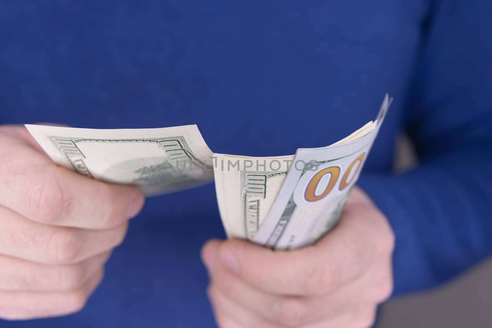 A man in a blue jumper holds a stack of 100 dollars in his hands close-up and counts them.Money concept. High quality photo