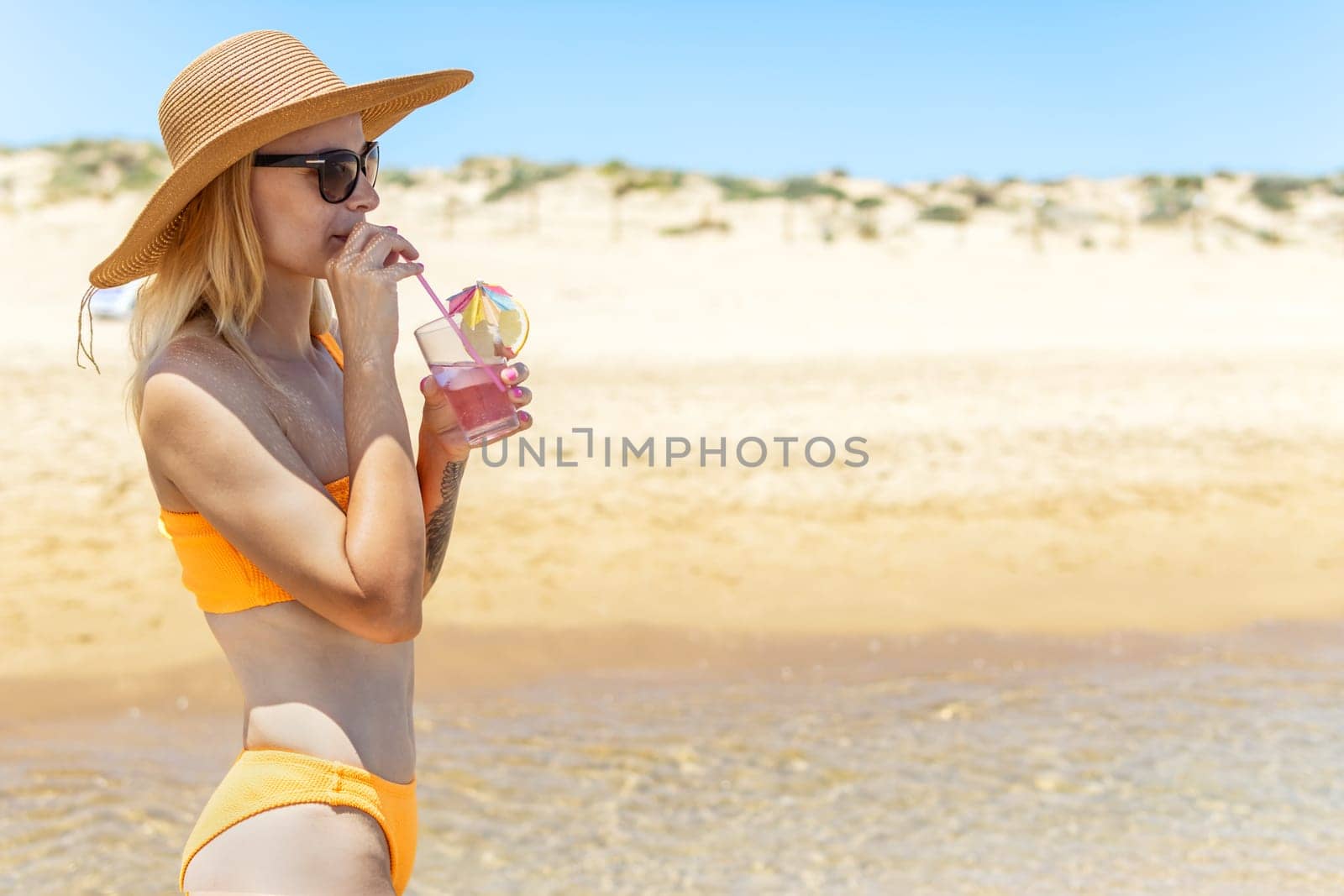 portrait of a girl in a swimsuit on the beach, standing on the shore and drinking a drink there is a place for an inscription. Photo of a sea landscape with a girl. High quality photo