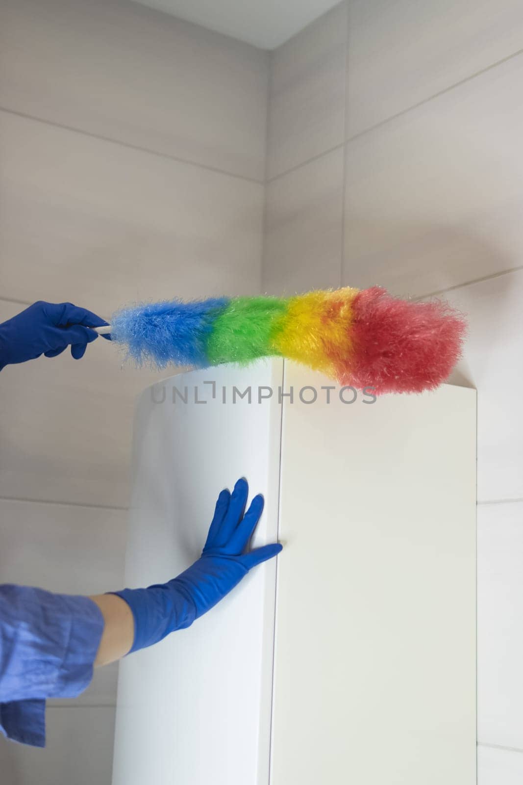 A girl in blue gloves and a blue shirt cleans the dust in the bathroom with a colored napkin, housekeeping concept