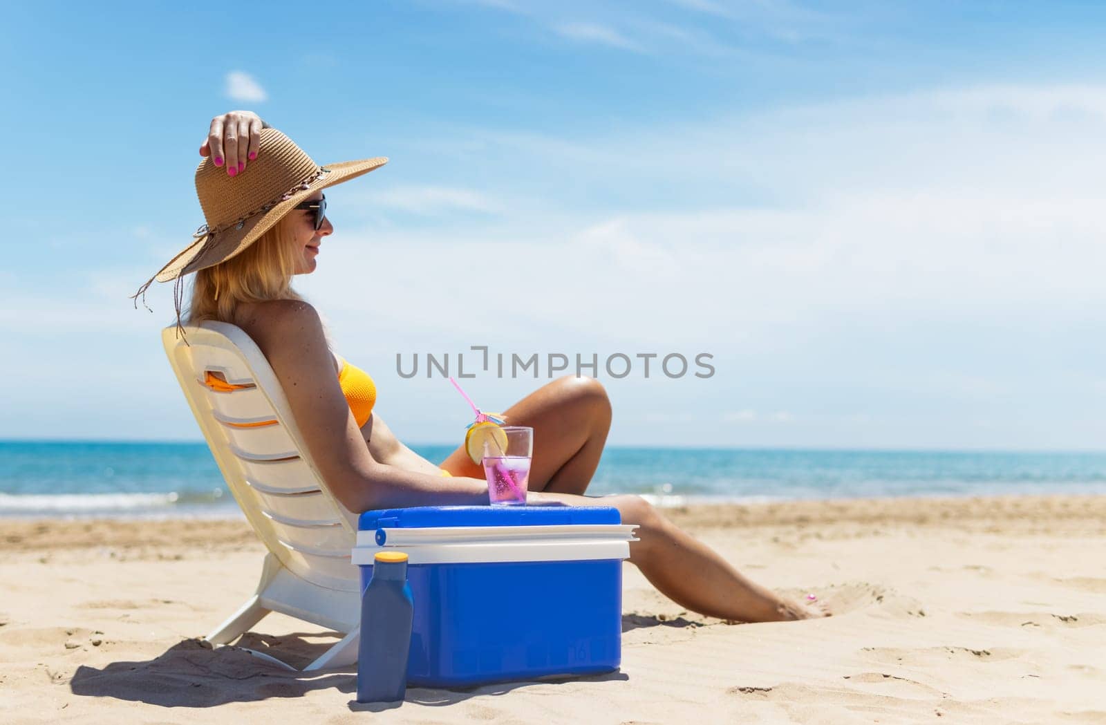 Happy young european girl drinks a cocktail and rests in a sun lounger on the beach, by PopOff