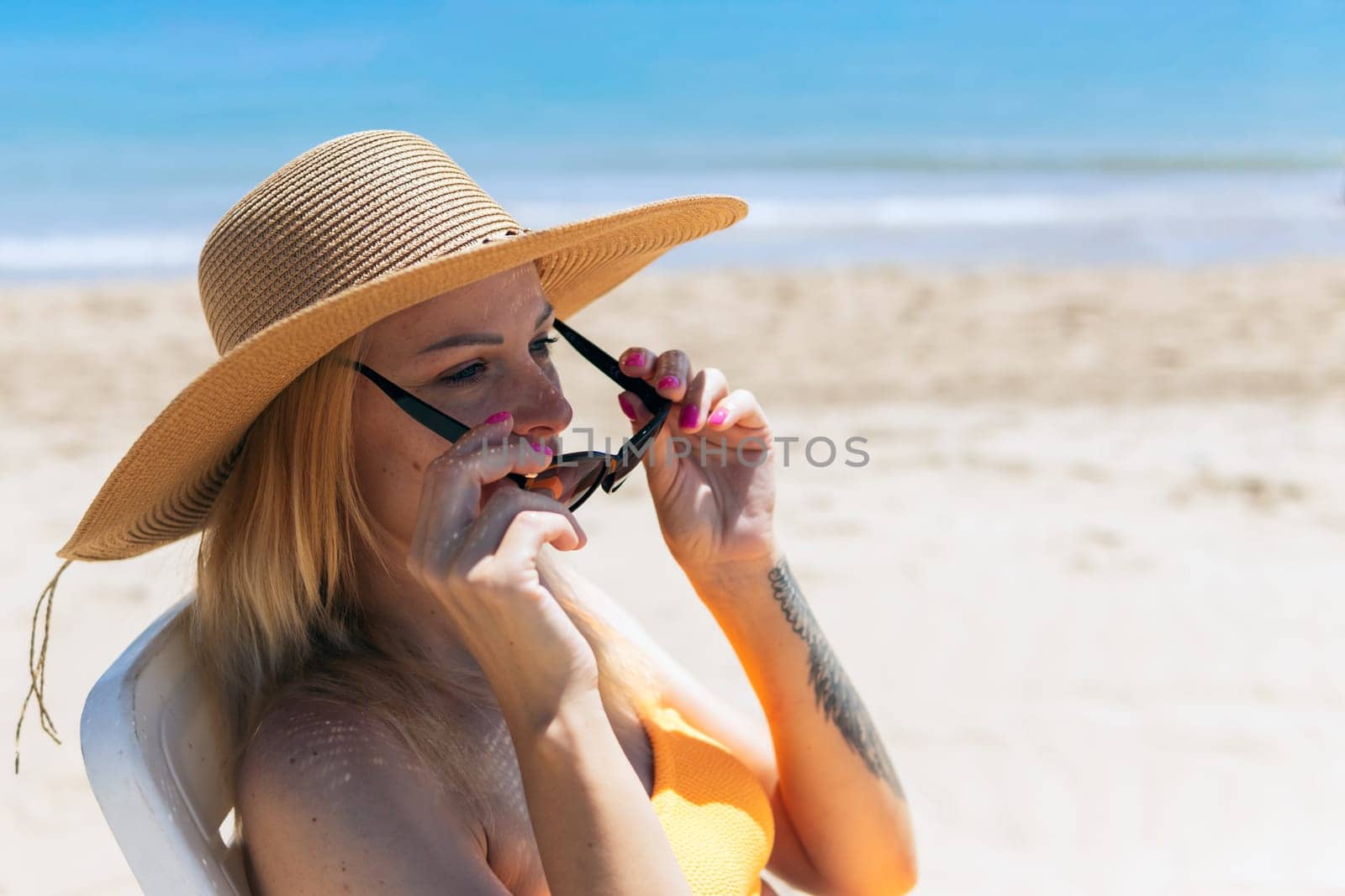 a sports girl in an orange swimsuit sits on a white sun lounger in a hat and glasses on the ocean, the concept of summer holidays, there is a place for an inscription. High quality photo