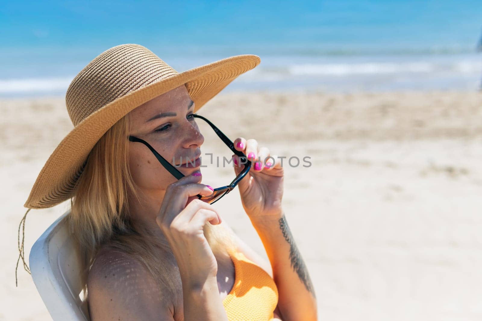 portrait of a beautiful tanned girl in a hat sitting on the beach, there is a place for an inscription, a beautiful seascape with a girl. High quality photo