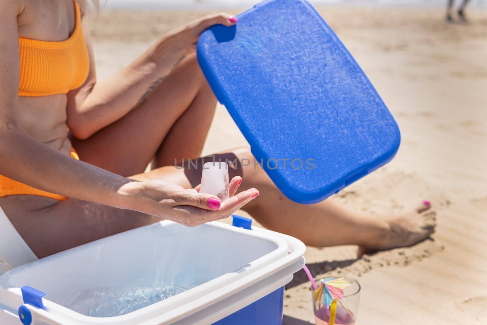 a girl in a bathing suit sits on the beach, takes out ice from a portable refrigerator. summer photo. High quality photo