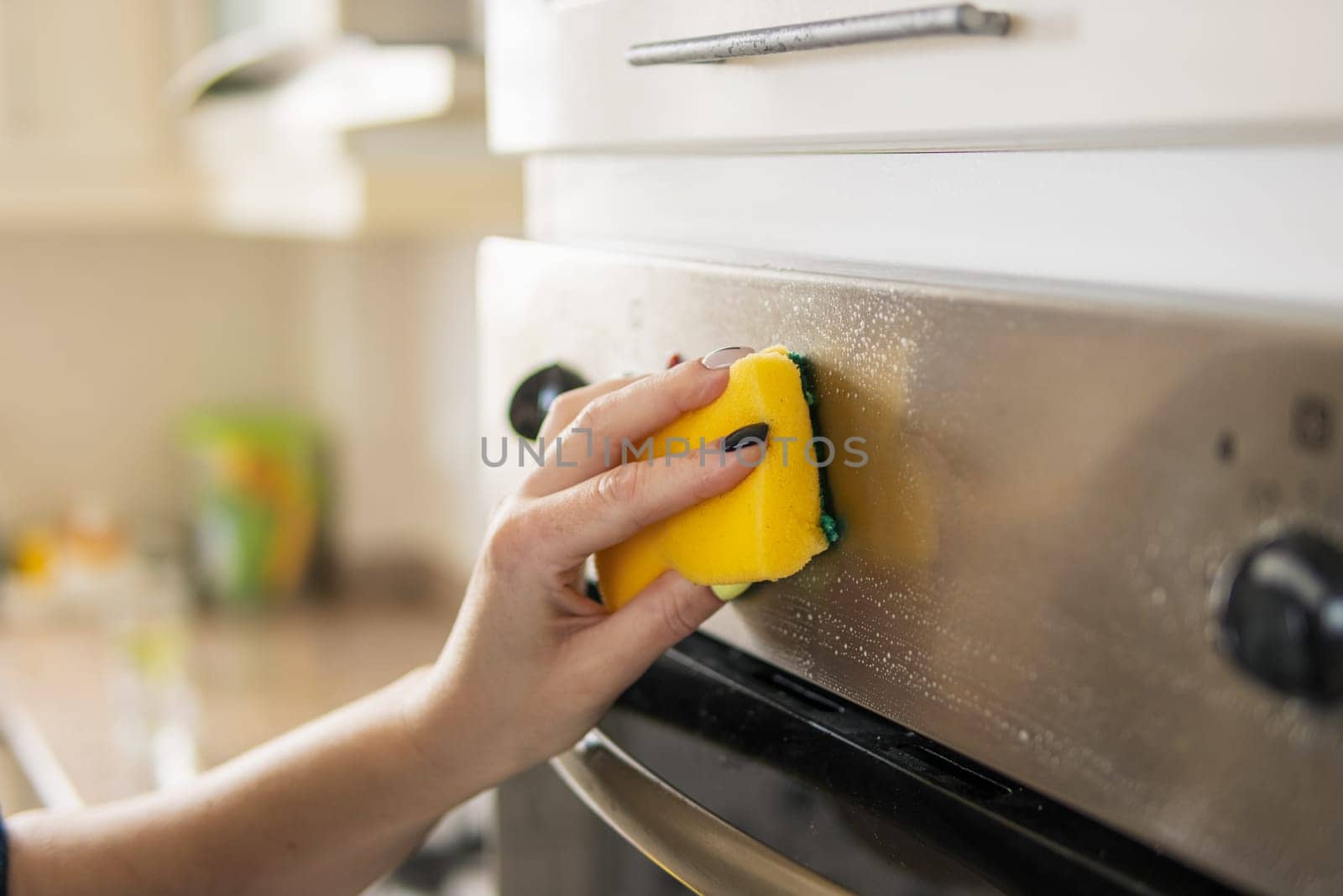 The girl washes the oven in the house with a yellow sponge, close-up, the background is blurred. The concept of cleaning. High quality photo