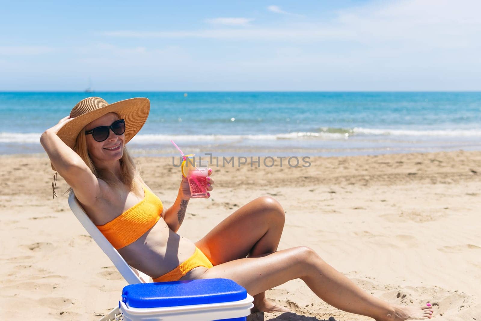 Happy young european girl drinks a cocktail and rests in a sun lounger on the beach, by PopOff