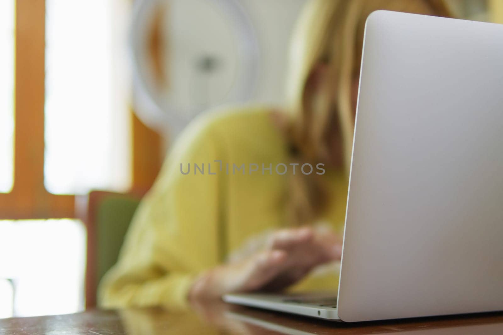 a girl in a yellow jacket sits in a room at a table and works on a laptop, the concept of remote work, there is a place for an inscription. High quality photo