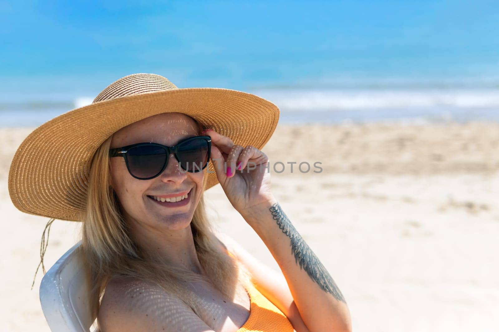Portrait of a happy european woman in an orange swimsuit sunbathing on a plastic sun lounger on a tropical beach, looking at the camera. High quality photo