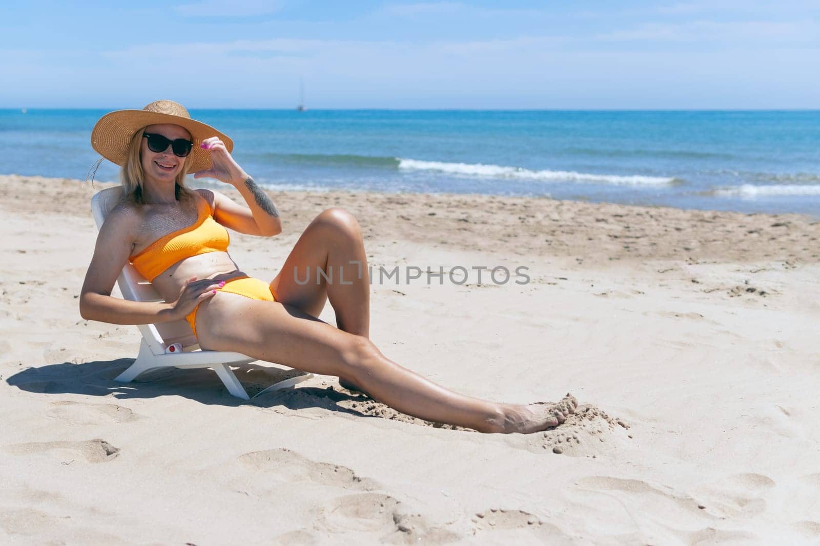 european girl in a hat and swimsuit relaxes and lies on a sun lounger on the beach alone, by PopOff