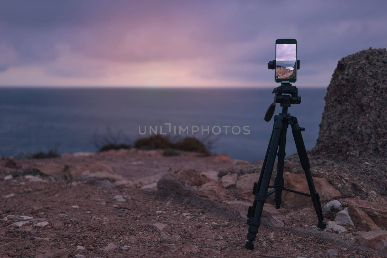 The smartphone camera is on a tripod, photographing a picturesque evening sunset over a tropical sea and a mountain. Photographing the sunset and sunrise of the natural landscape. High quality photo
