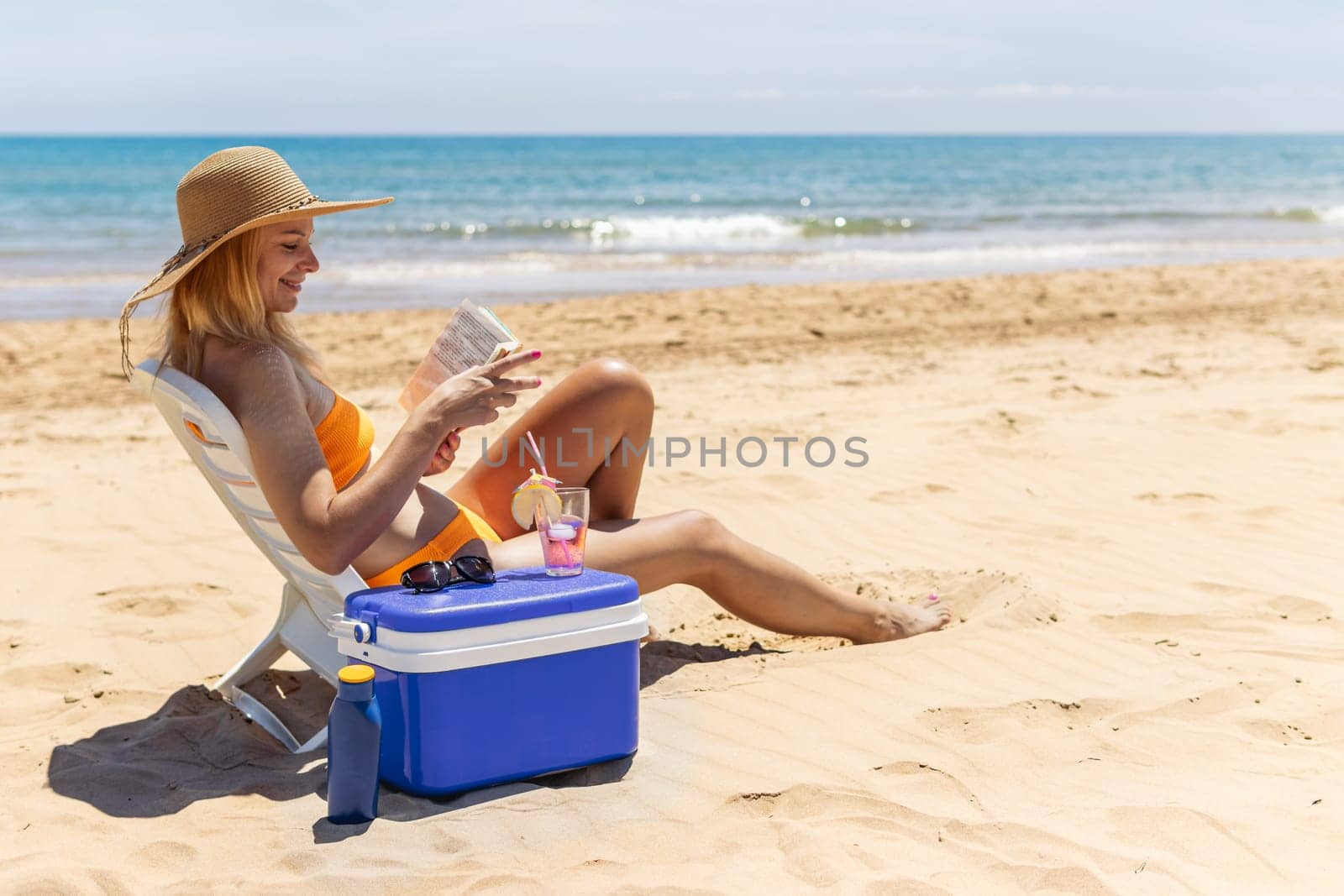 happy girl sits on the beach in a swimsuit reads a book and drinks a cocktail.beautiful seascape with a girl with a place for an inscription. High quality photo