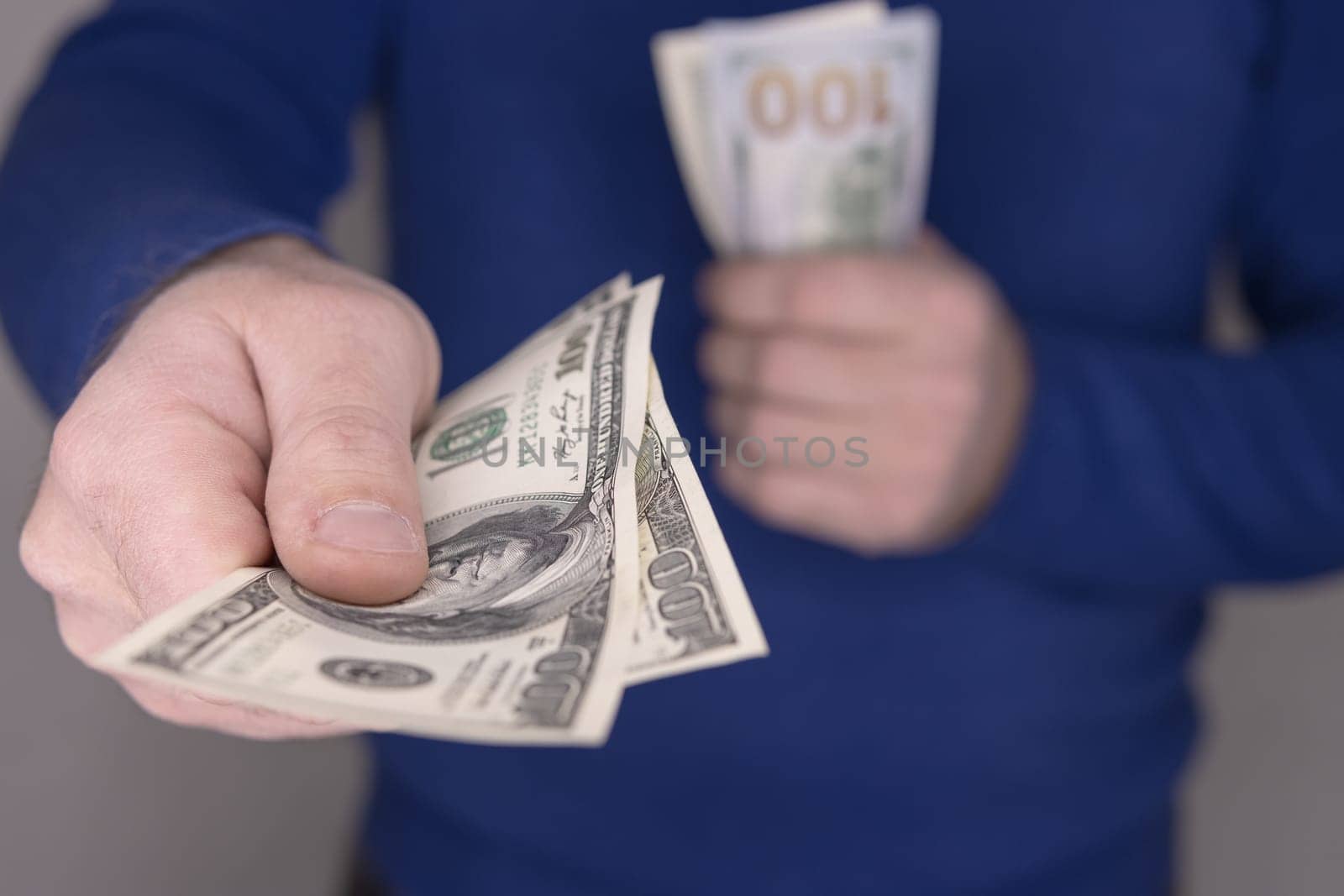 A man in a blue jumper holds money in his hands, a stack of 100 dollars blurred and close-up of money 100 dollars 200 dollars.Money concept. High quality photo