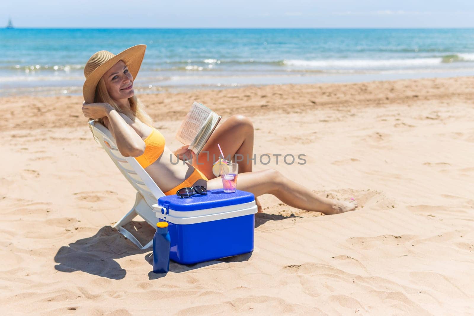 a slender girl in a swimsuit sits on a sun lounger sunbathes and reads a book on the beach by PopOff