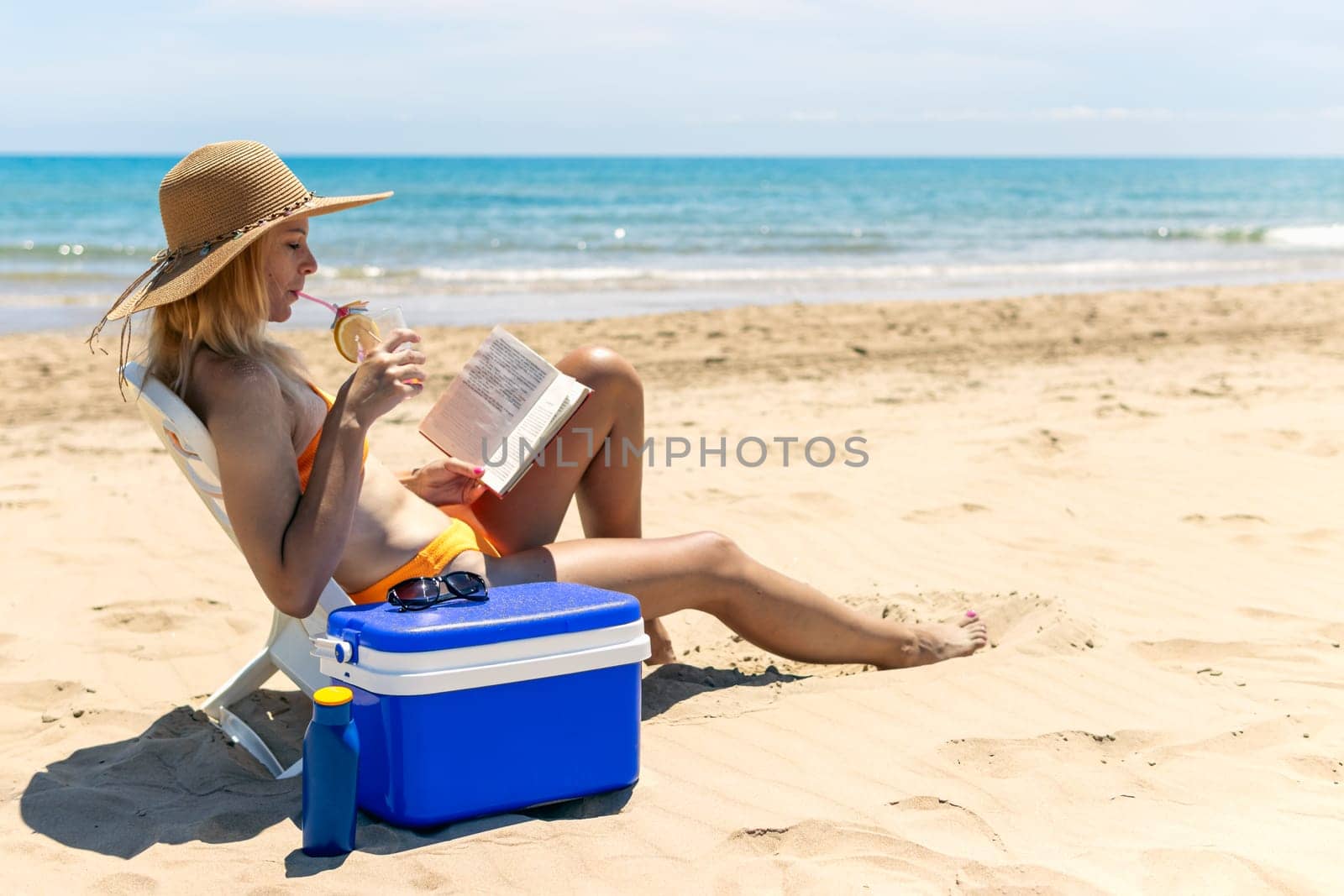 a girl of European appearance is sitting on the beach in a bathing suit reading a book and drinking a cocktail. a beautiful sea landscape with a girl. High quality photo