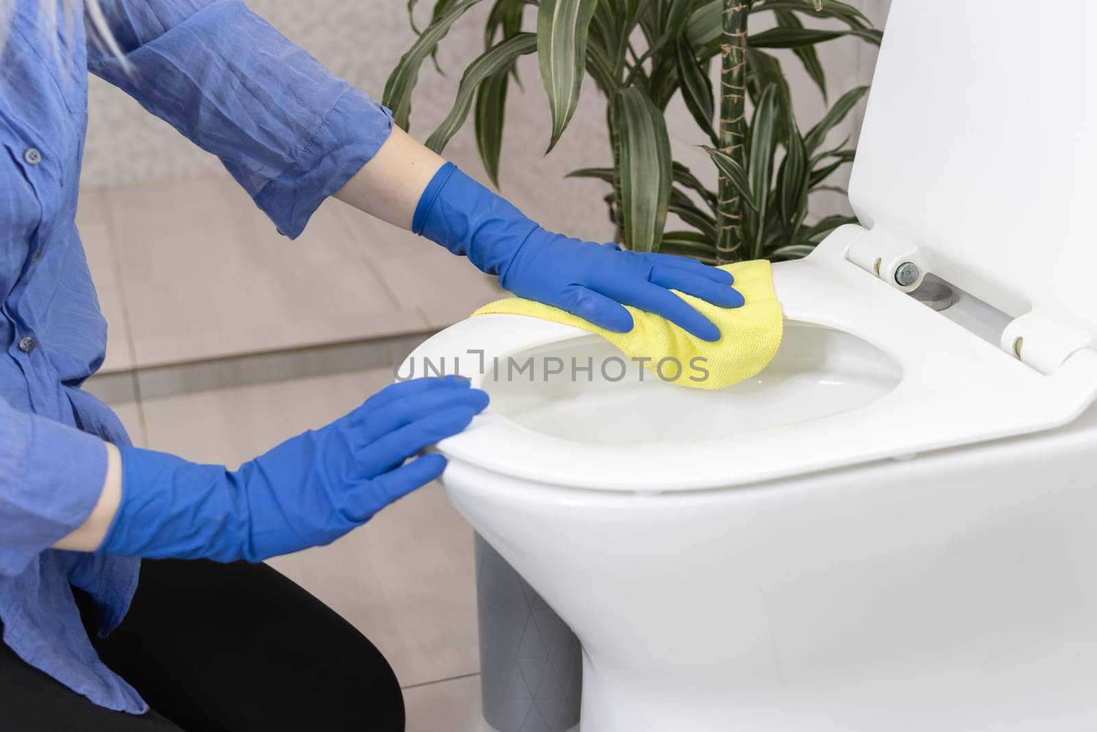 a girl of European appearance with fair hair in blue gloves is cleaning the bathroom in the house and cleans the toilet bowl with a yellow napkin