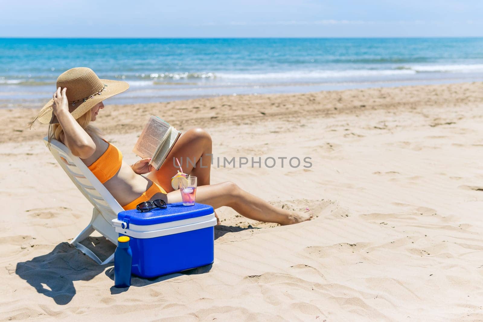 happy girl sits on the beach in a swimsuit reads a book and drinks a cocktail.beautiful seascape with a girl with a place for an inscription. High quality photo