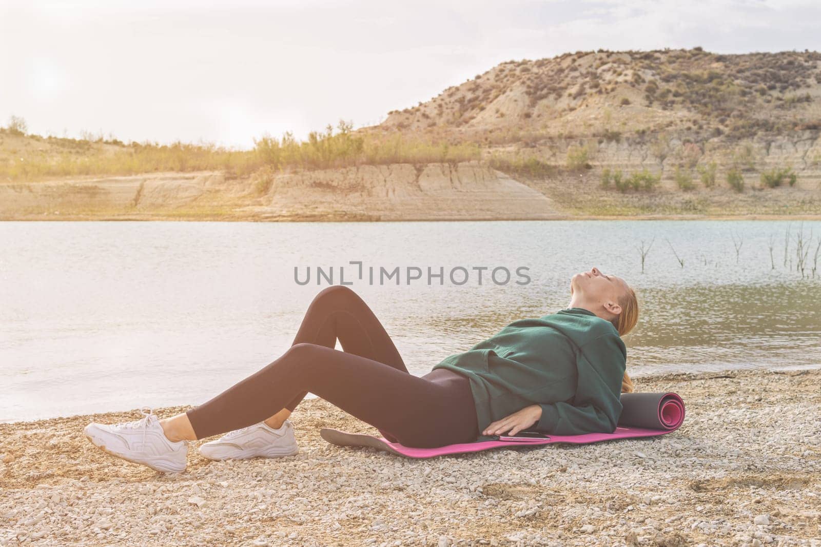 a girl of European appearance in sportswear lies on a yoga mat near a beautiful lake. Beautiful landscape of nature, there is a place for an inscription. Lake with turquoise water. High quality photo