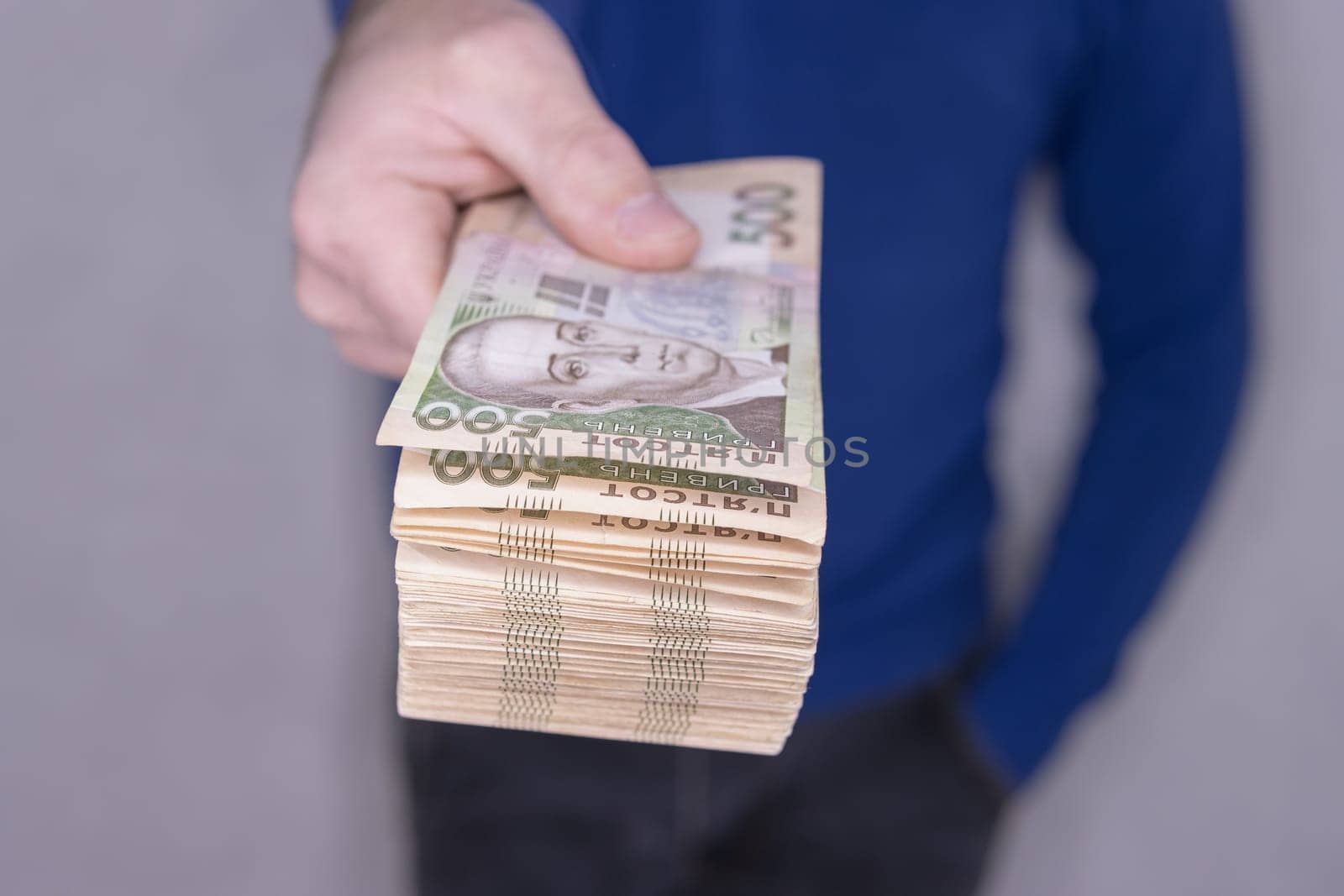 A man in a blue sweater holds a stack of new banknotes of the Ukrainian hryvnia in his hands 500 hryvnia.On a light background.500 hryvnia. High quality photo.Finance concept