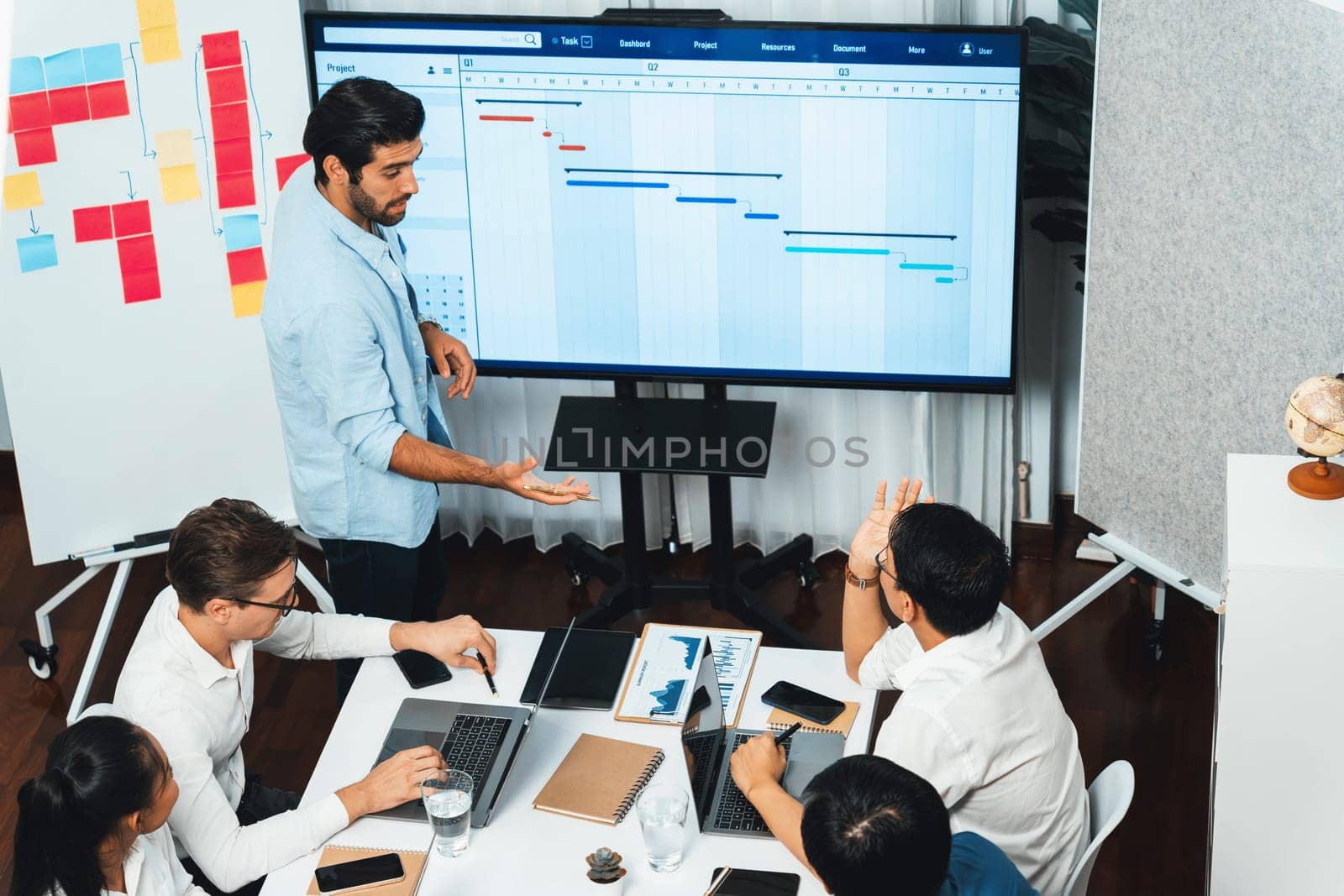 Project manager communicate and collaborate with team using project management software display on monitor, tracking progress of project task and making schedule plan at meeting table. Prudent