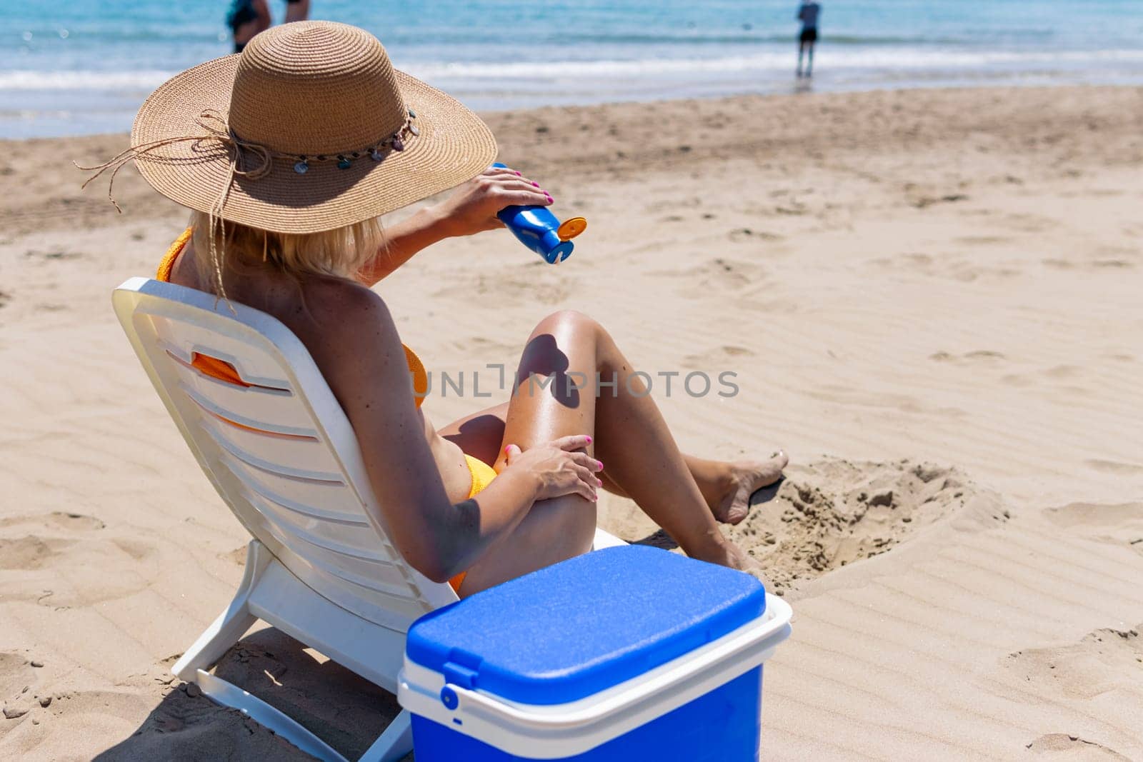 the girl is holding a blue bottle of sunblock cream in her hands on the beach, the girl is sitting on a sun lounger in a swimsuit. High quality photo