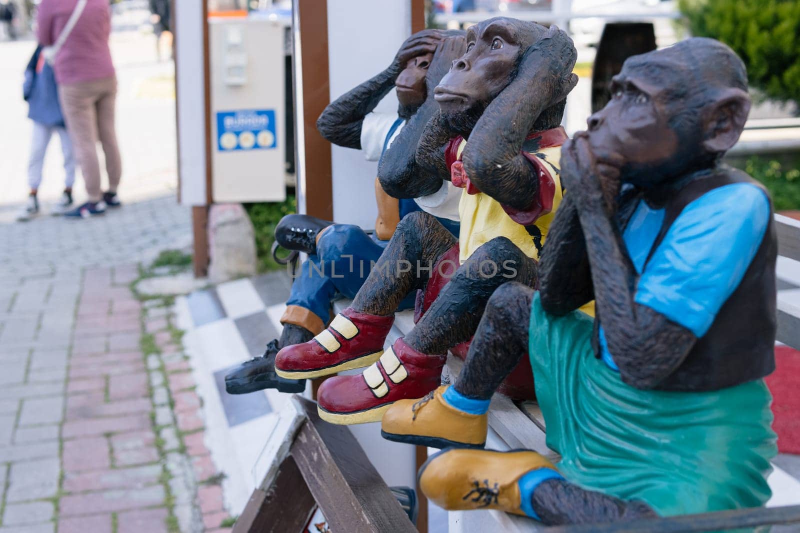figures of three monkeys in clothes sitting on a bench on the street, funny figures. High quality photo