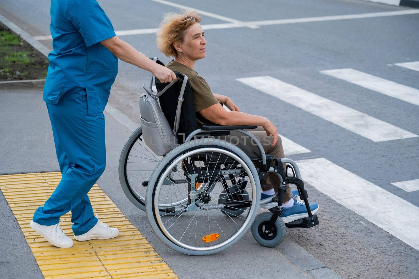 Profile of a nurse helping an elderly woman in a wheelchair cross the road. by mrwed54