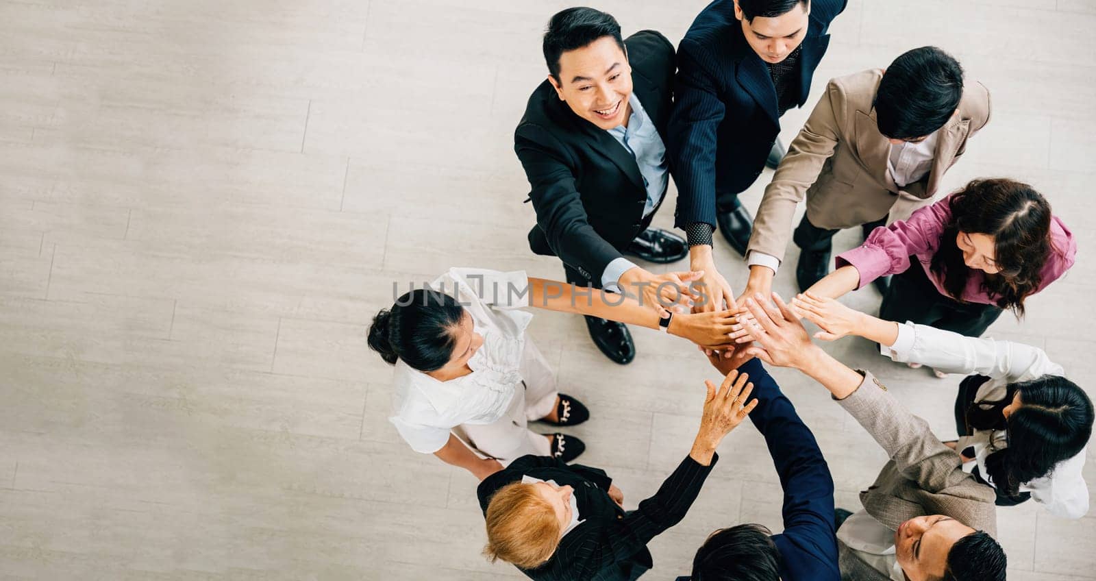 An overhead shot captures four diverse business colleagues in a unity circle stacking their hands. This symbolizes teamwork success and global cooperation in the corporate world. by Sorapop