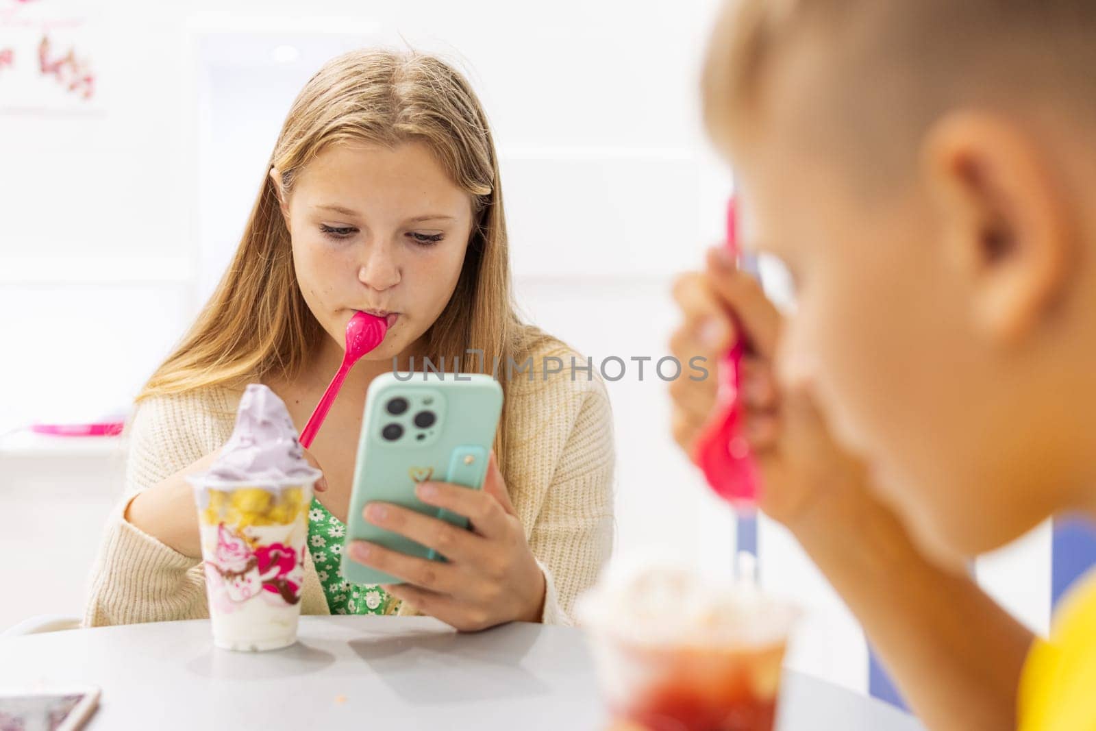 boy and a girl eat ice cream in a summer cafe in a summer cafe,a girl looks at a photo on her phone by PopOff