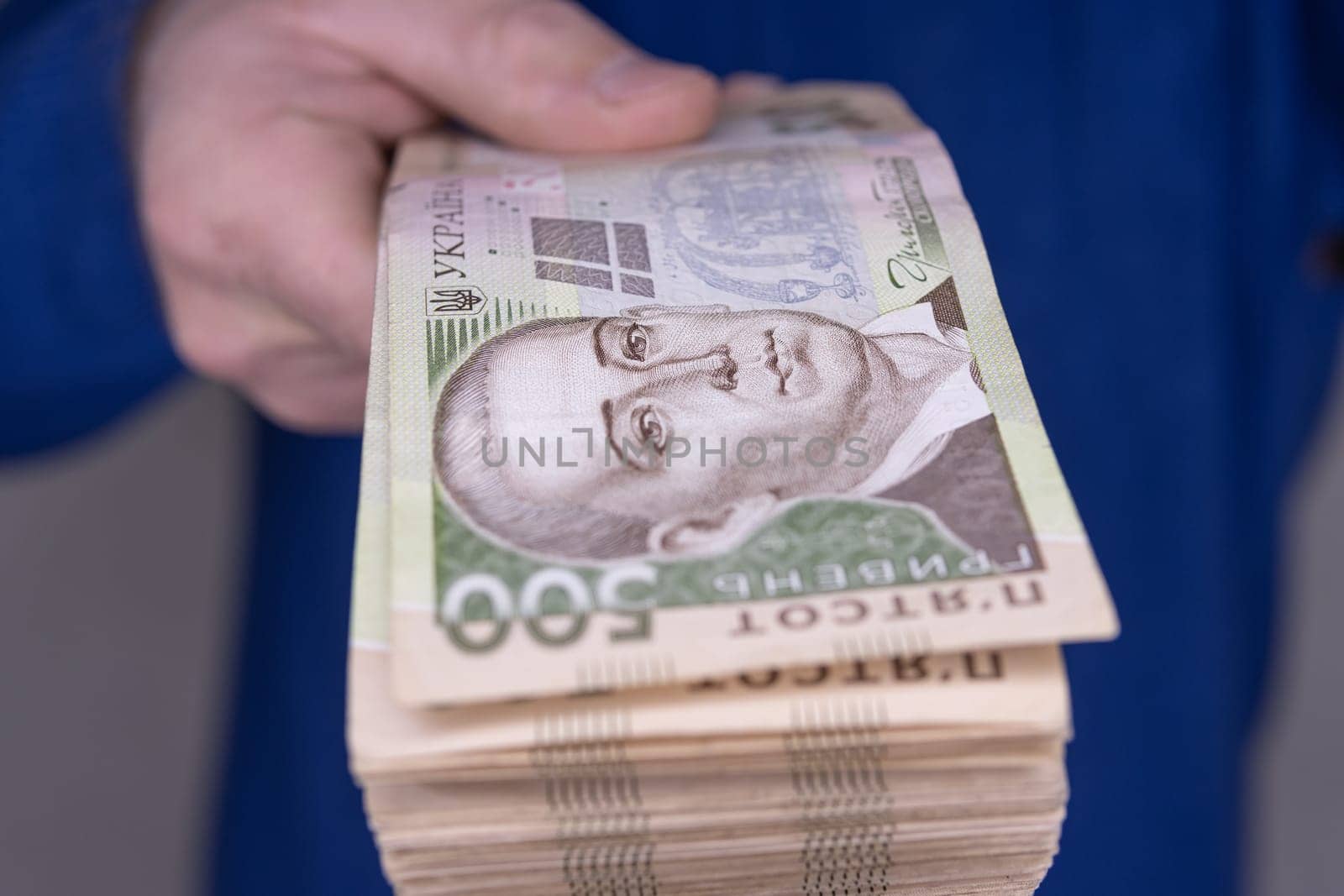 A man in a blue sweater holds a stack of new banknotes of the Ukrainian hryvnia in his hands 500 hryvnia close-up.On a light background.500 hryvnia close-up. High quality photo.Finance concept