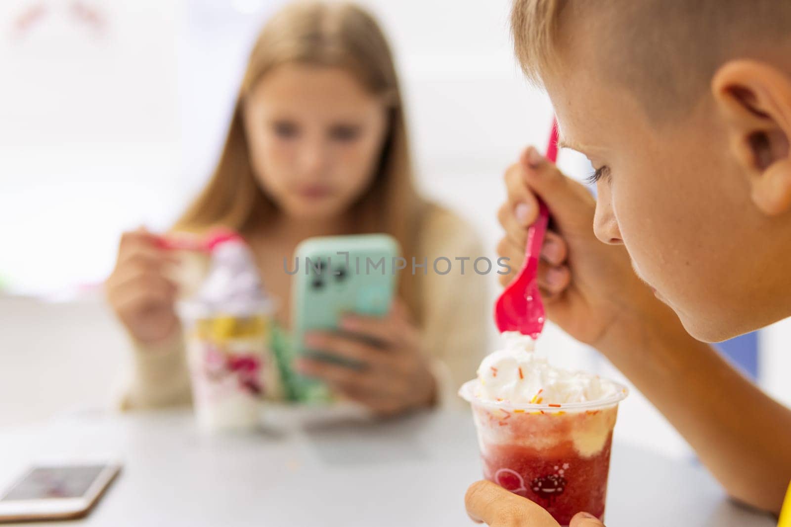 brother and sister are sitting in a cafe, eating ice cream and a girl is looking at a message on the phone, the concept of a summer family vacation. High quality photo