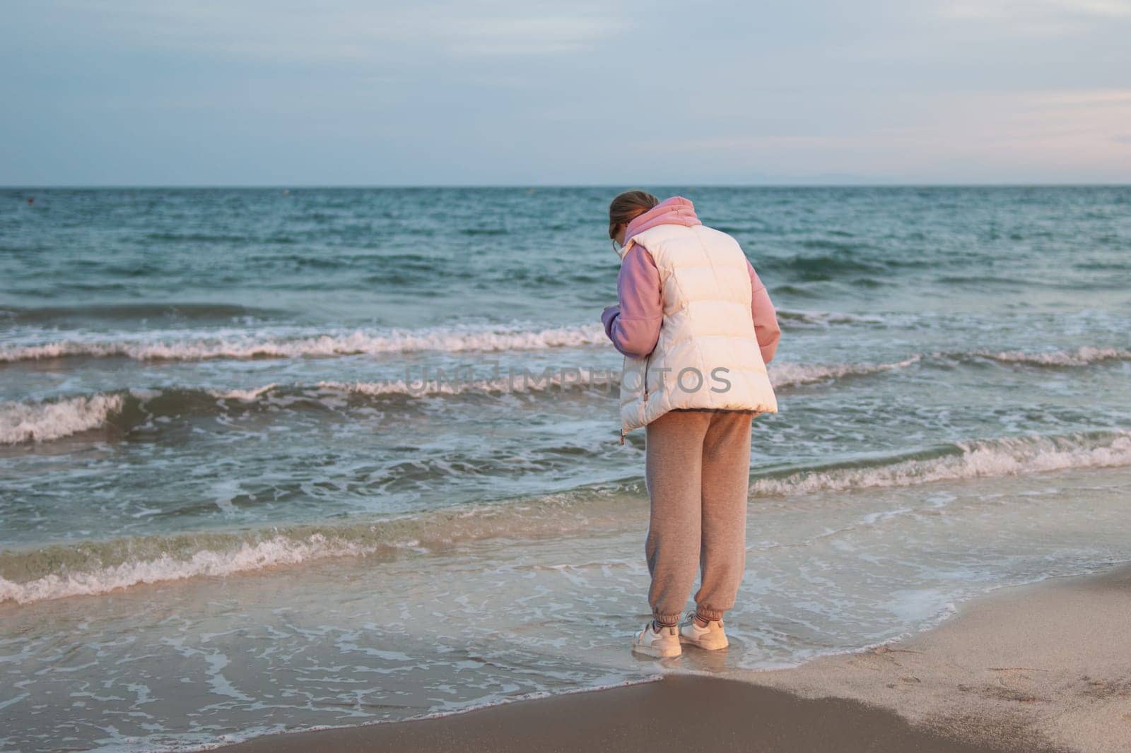 A young girl standing alone near the coast of the sea ocean. Fresh spring morning and dramatic sky. by PopOff