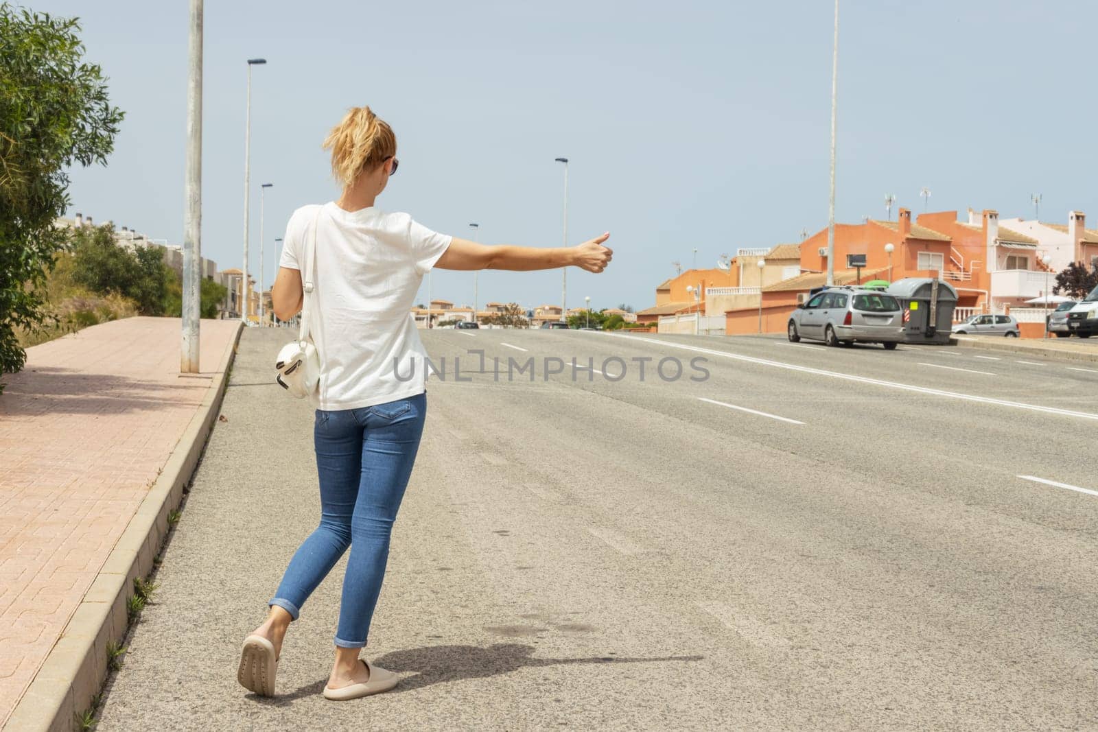 girl in casual clothes stands on the road with her back to the camera and stops the car on the road by PopOff