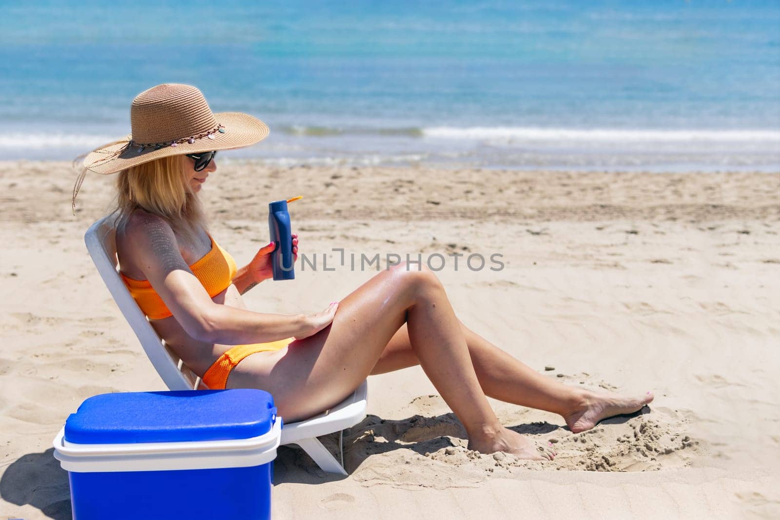 A woman smears sunscreen with moisturizing lotion on her smooth tanned legs. The girl is holding sunscreen. High quality photo