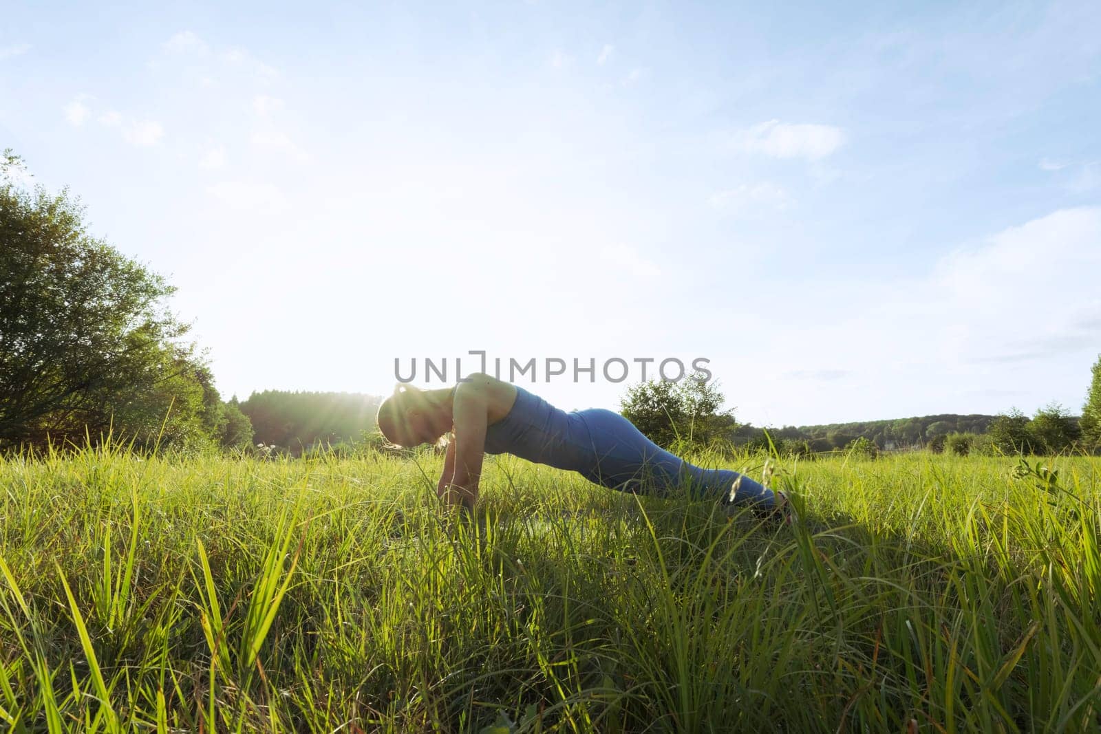 girl in a blue suit for fitness in the fresh air at sunset in the park goes in for sports, stands in the bar. There is green grass,the landscape is beautiful. The concept of sports. High quality photo