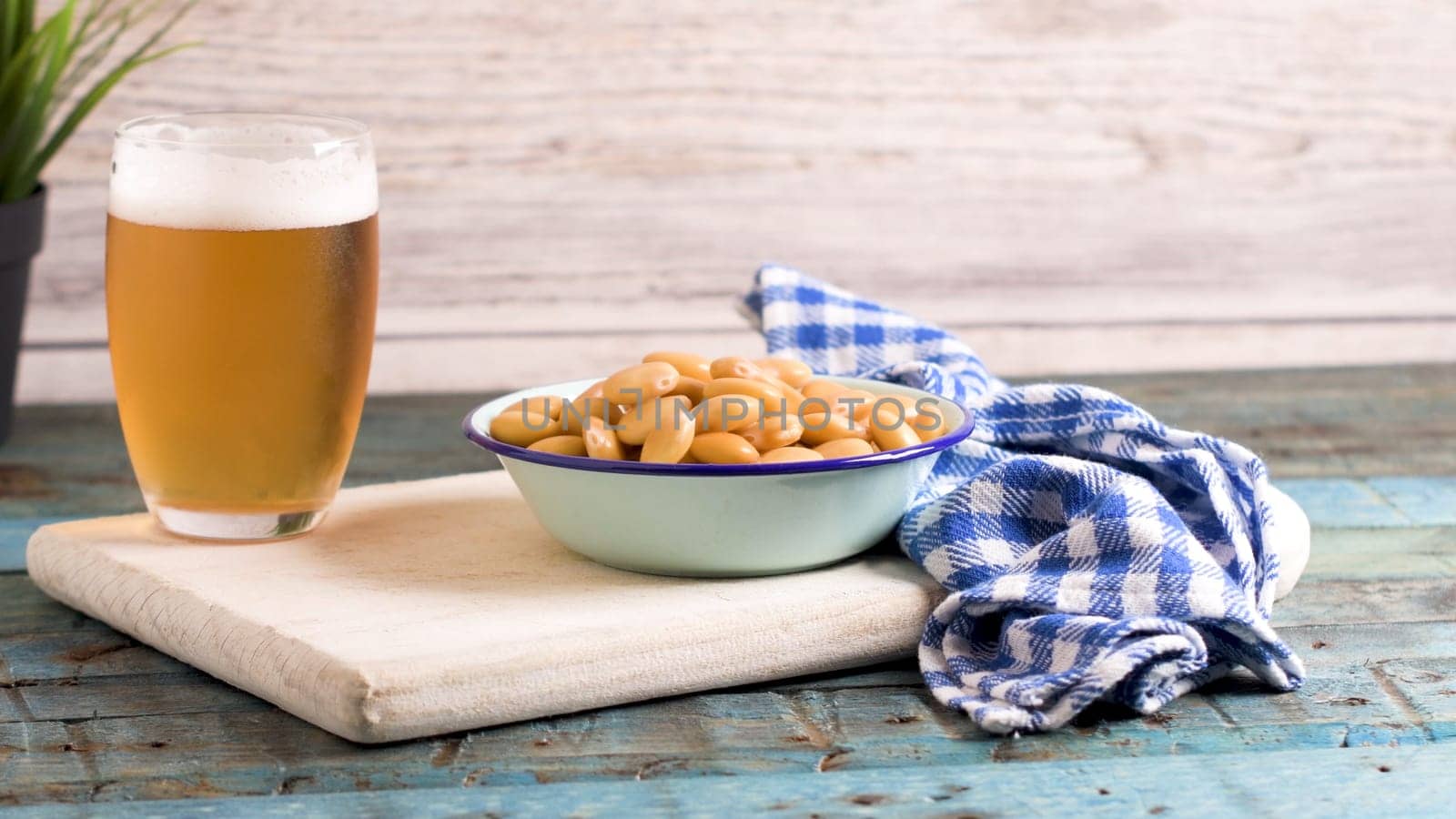 Tasty lupins in metal mug and glass of beer on wooden table top.