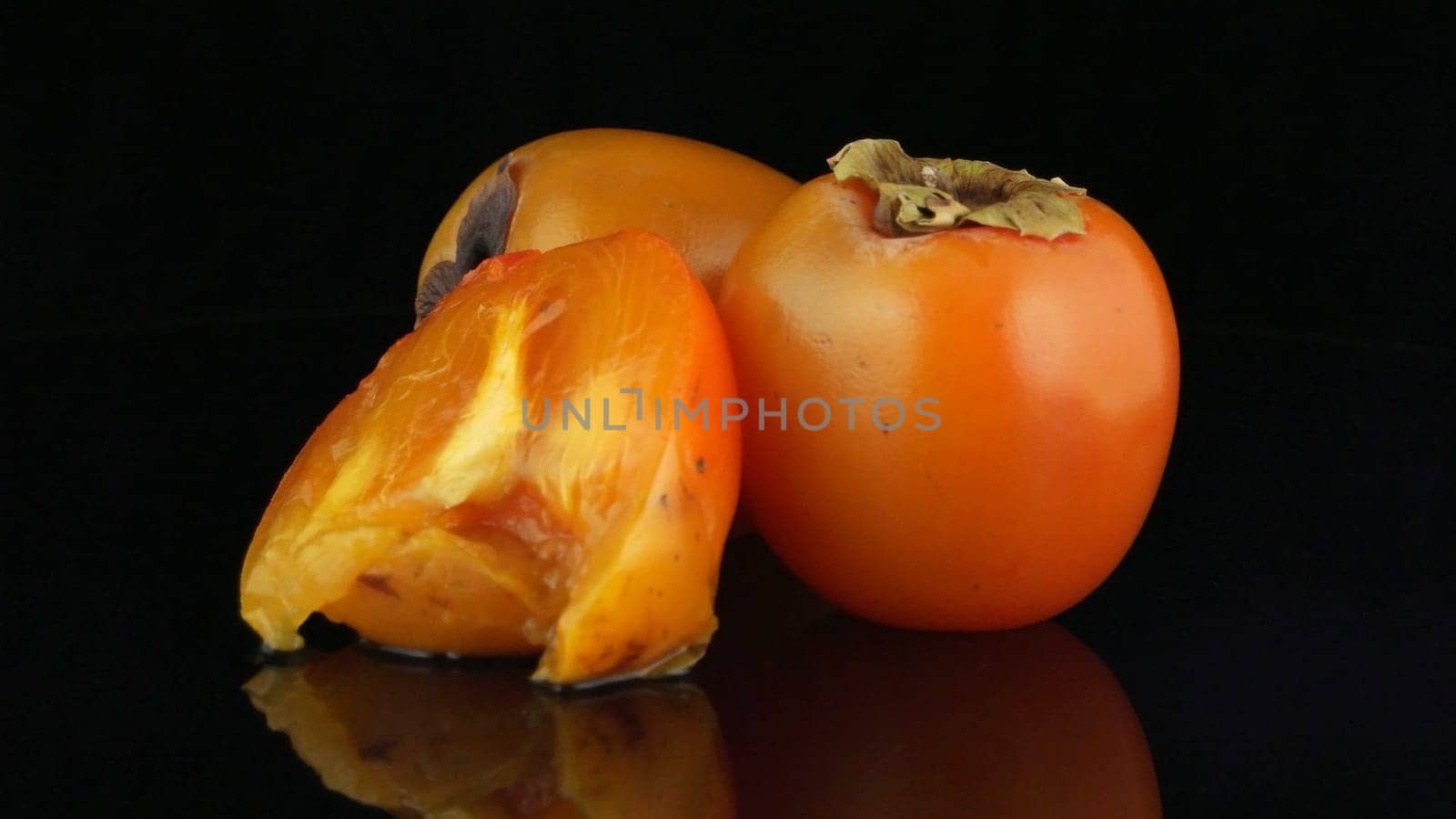 Red ripe persimmons rotating over black background.