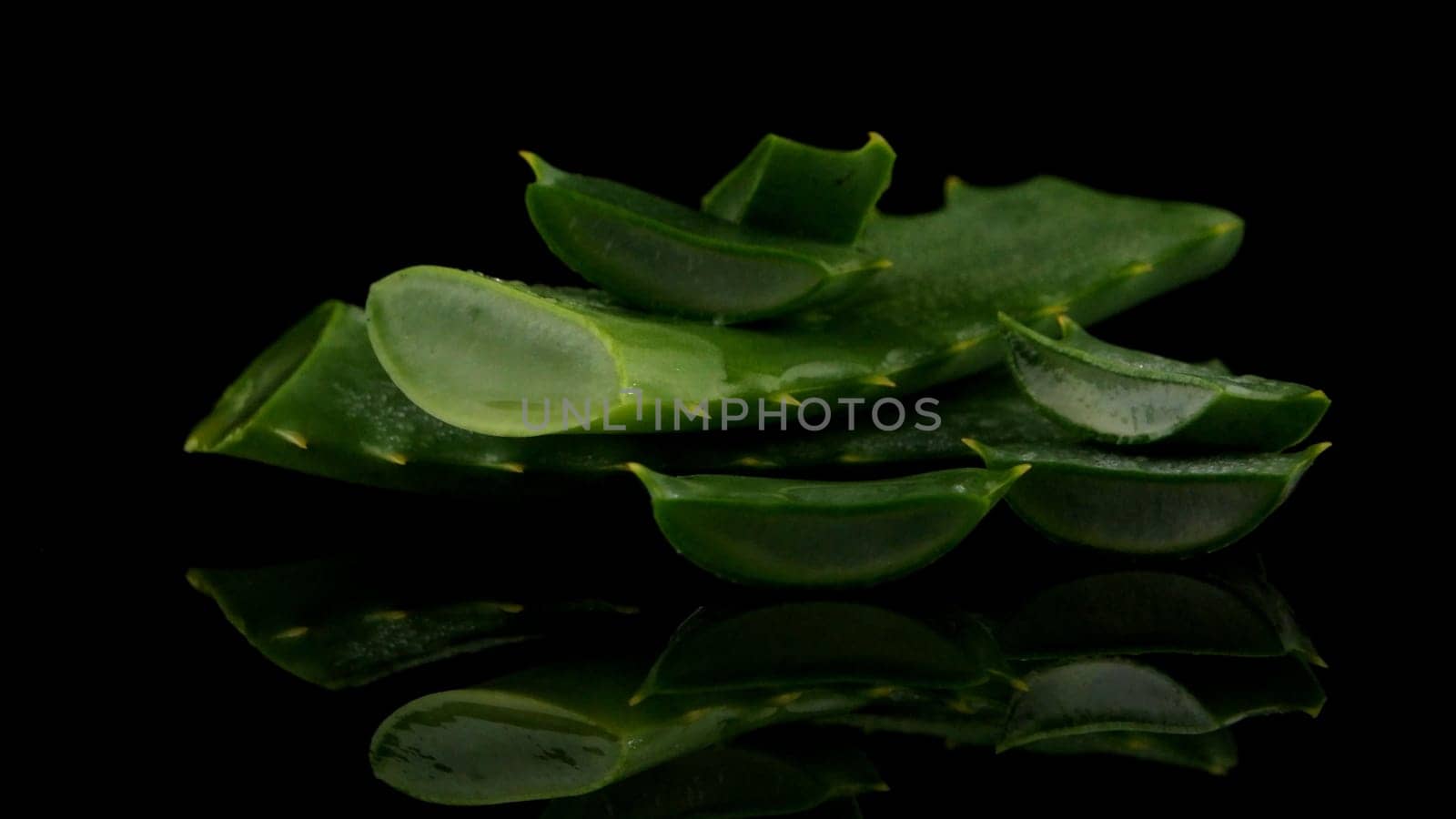 Sliced aloe leaf and water drops isolated on black background.