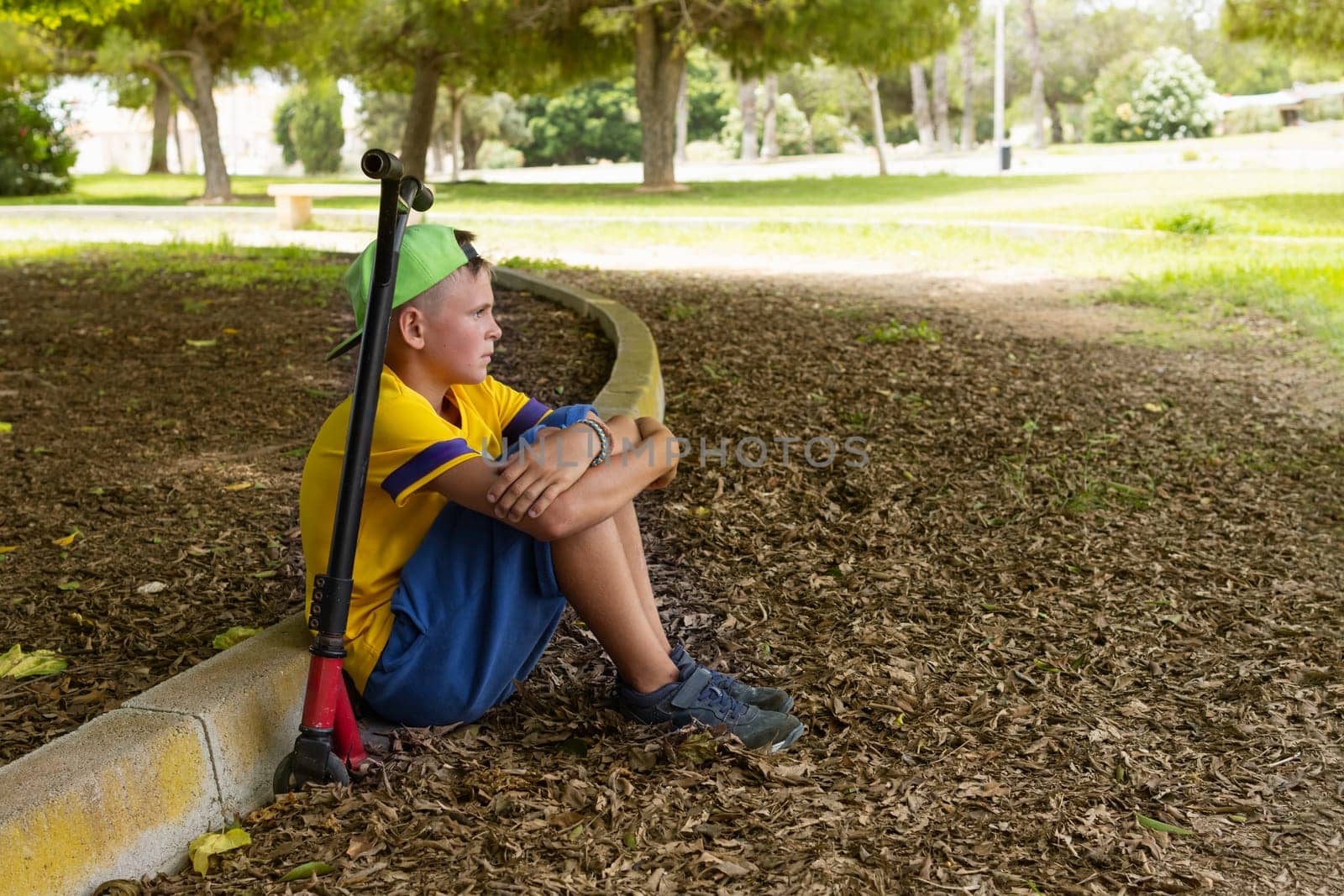 teenager in casual clothes sitting in the park on a scooter relaxing, active lifestyle of a child. High quality photo