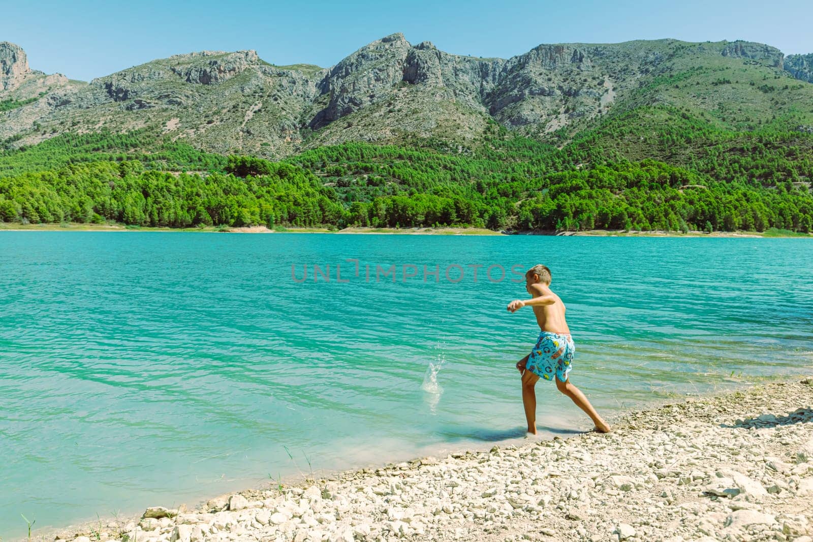 A teenager in shorts walks near a mountain lake against the backdrop of a beautiful landscape beautiful mountain landscape with a child against the backdrop of mountains and a lake. High quality photo