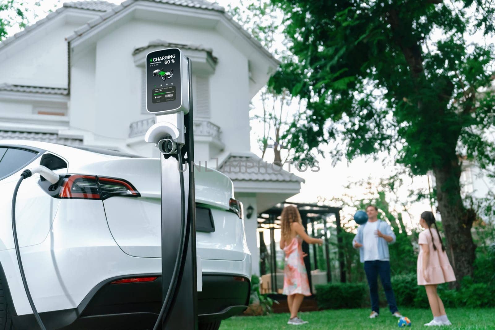 Focus EV station recharging battery for EV car on blurred family. Synchronos by biancoblue