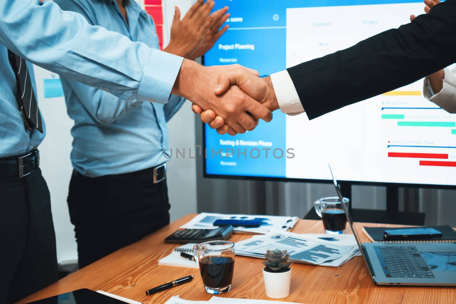 Cheerful meeting room, businesspeople celebrate with handshaking. Successful project was completed before the deadline. Business partnership and collaboration in project management. Habiliment