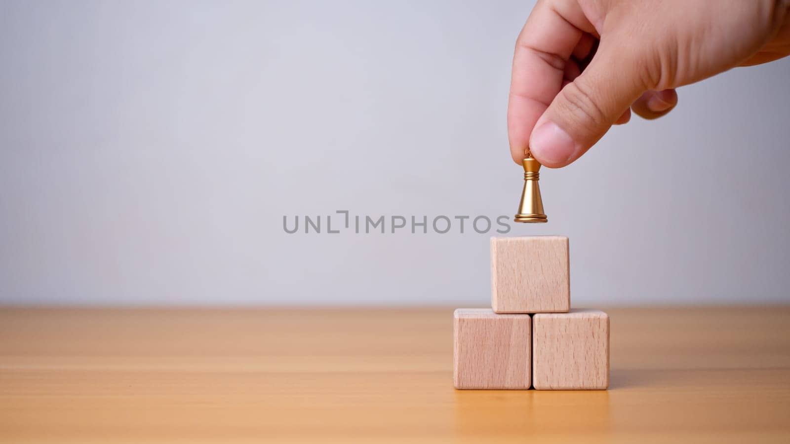 Businessman's hand holding a king placed on the topmost layer of wood. It represents the concept of competition and strategic adjustments for competitors in the business. by Unimages2527