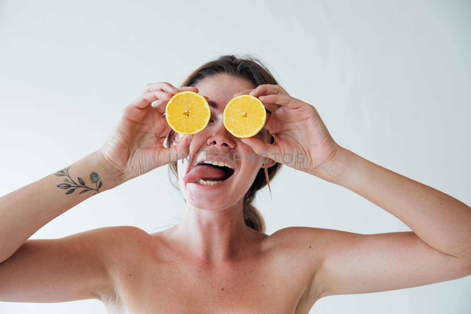 woman with oranges by her eyes shows her tongue