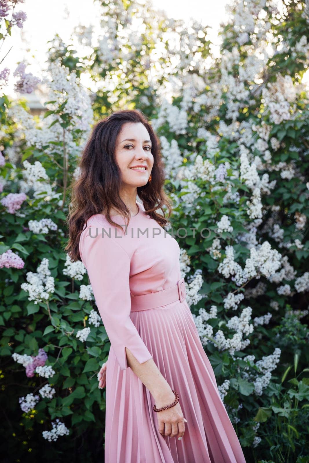 beautiful woman in a pink dress stands near a large lilac bush