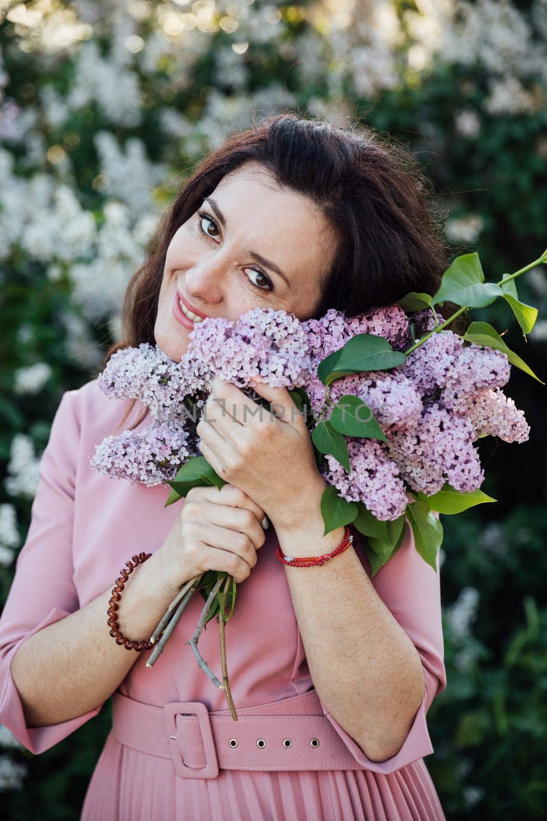 beautiful woman in a pink dress stands with lilacs in her hands