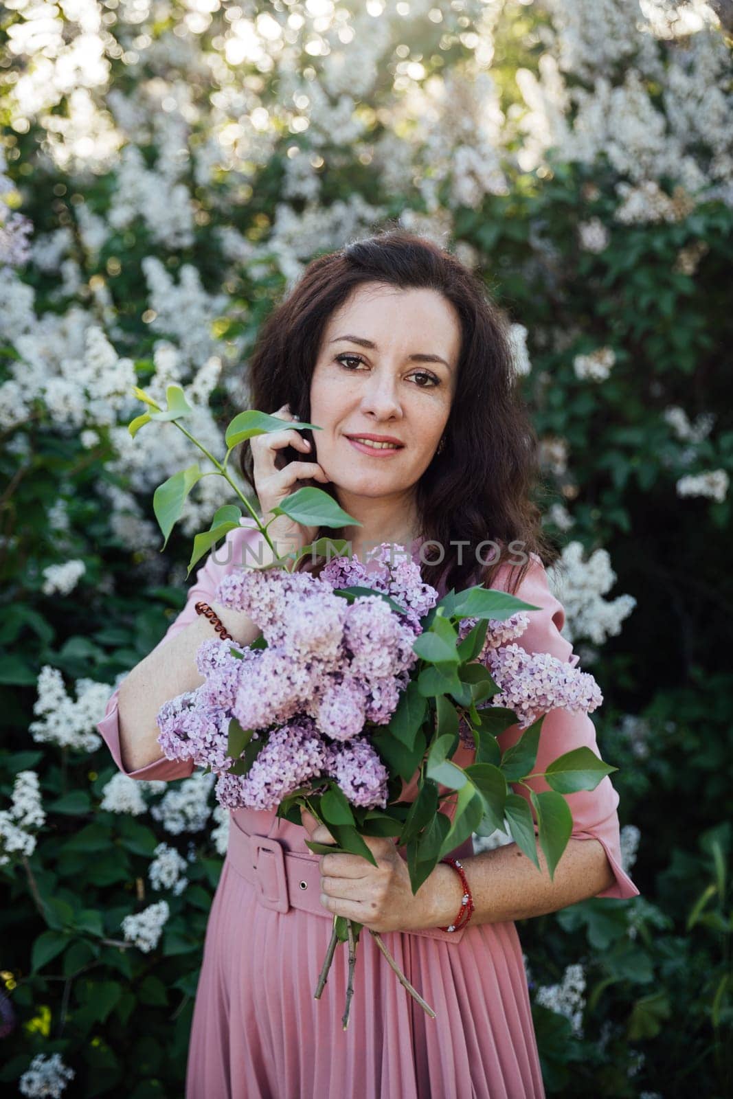 a beautiful woman in a pink dress stands with lilacs in her hands by Simakov