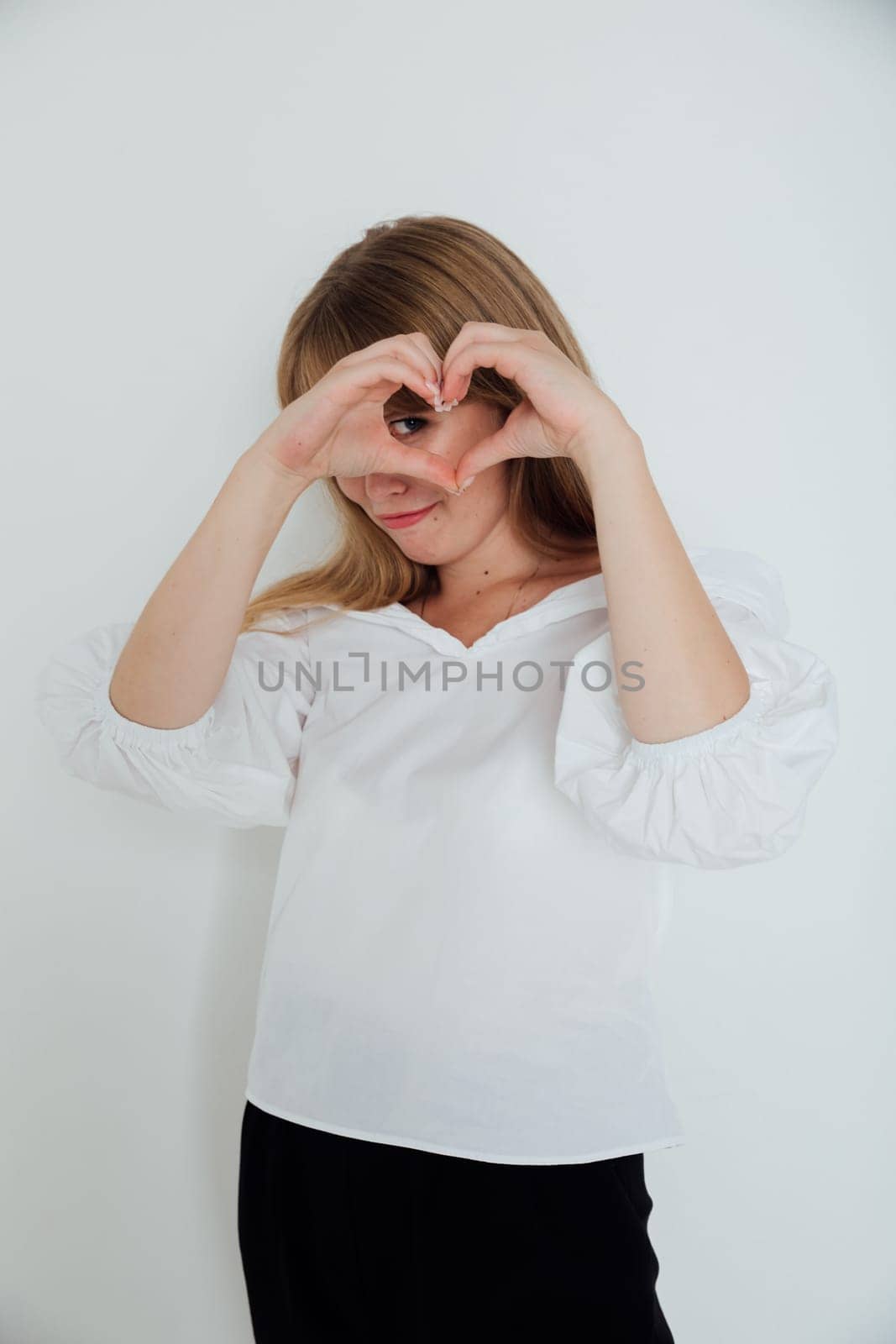 woman in white made a heart out of her fingers and looks into it
