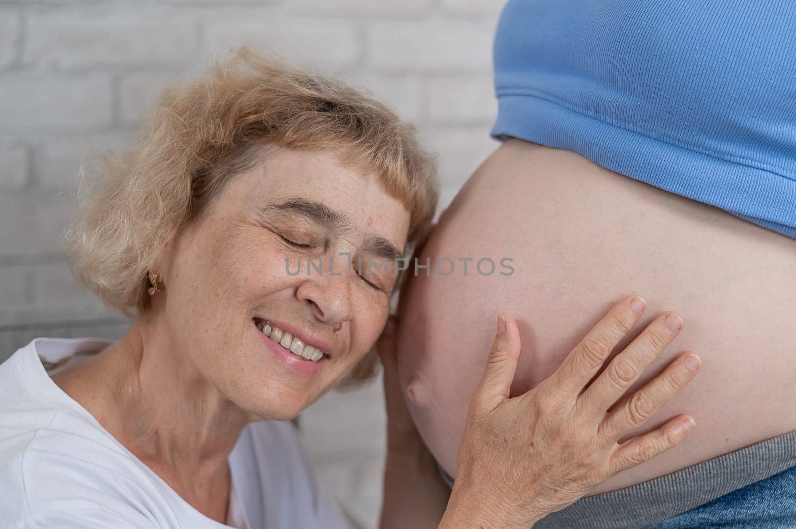 An elderly woman leans against the belly of her pregnant daughter. Close-up