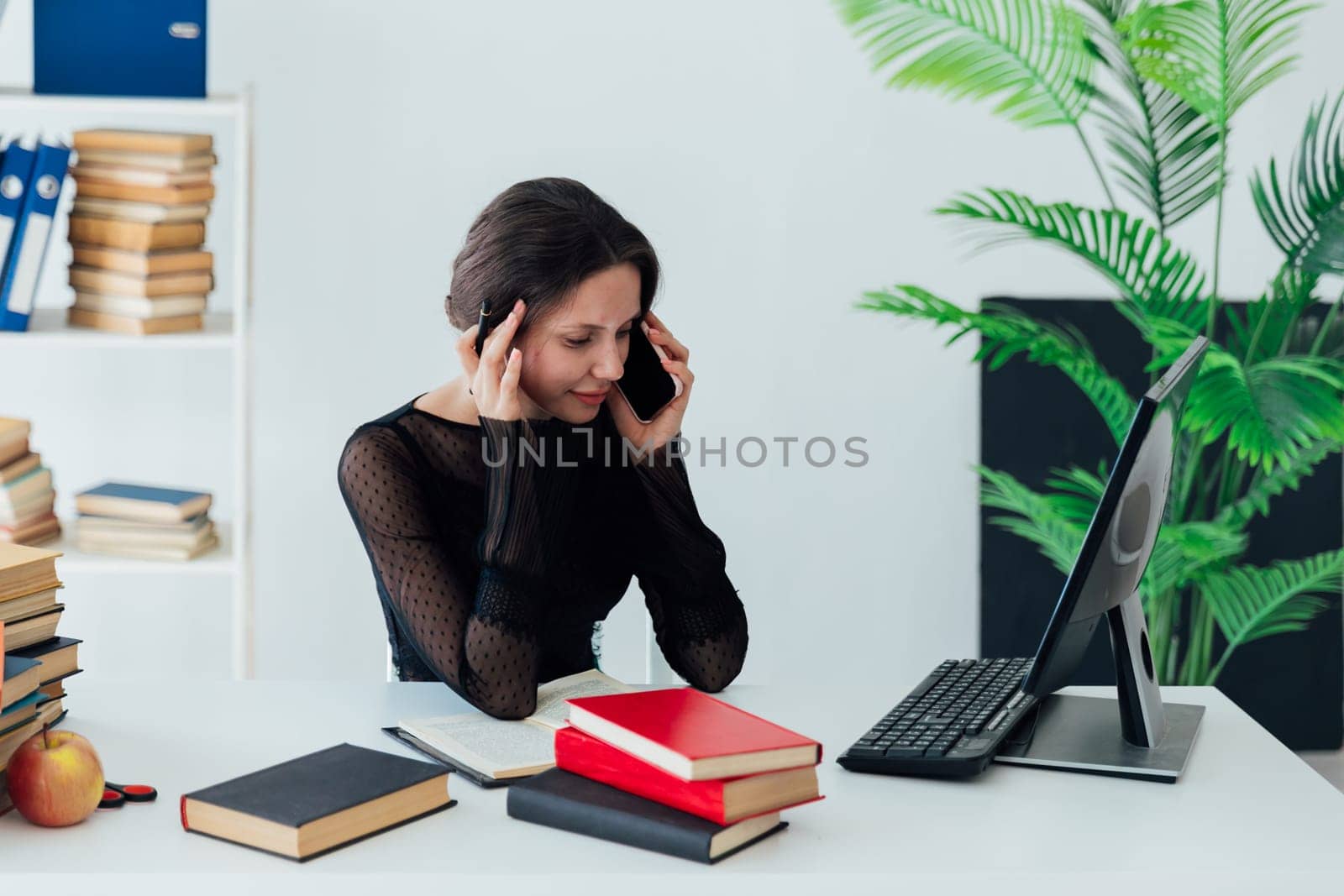 a business woman in an office at a desk near books is on the phone by Simakov