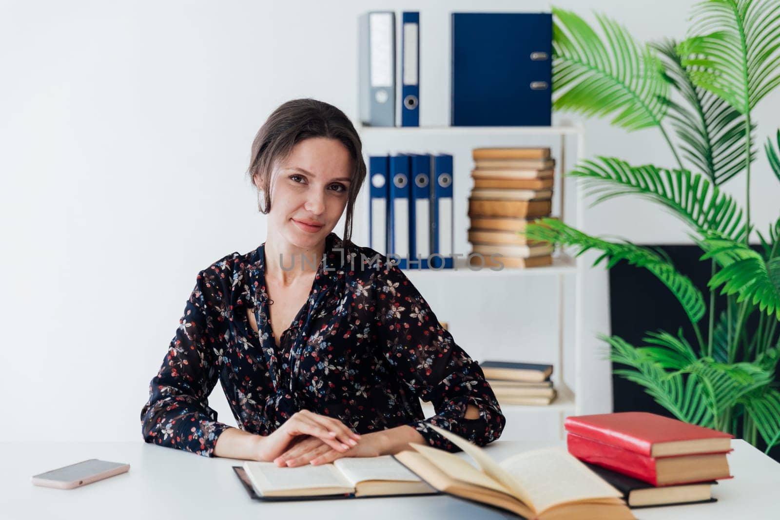 business woman sits in an office with a stack of books